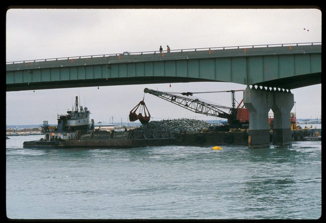 This 1989 image shows efforts to place a blanket of rocks along the bottom of the Indian River Inlet to offset scouring and support the previous bridge's in-water structures.